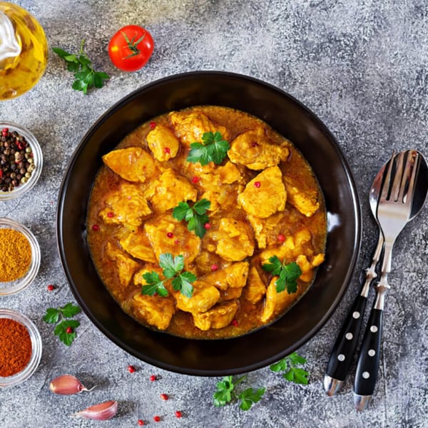 Annapurna Cuisine's Indian chicken curry in a black bowl, garnished with parsley and red peppercorns.