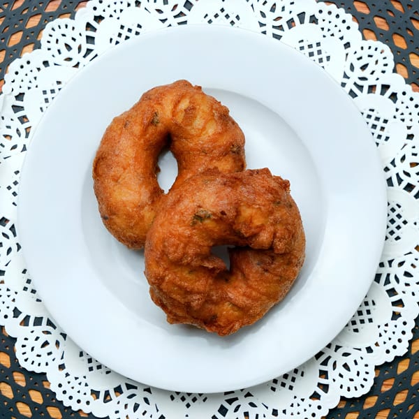 Two golden-brown, ring-shaped Indian medu vada on a white plate with a doily.