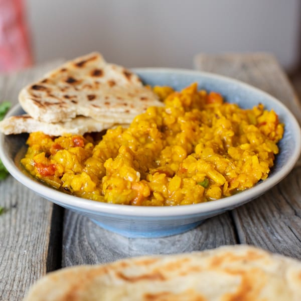 A blue bowl of Annapurna Cuisine's yellow Indian dal with flatbread on a rustic wooden table.