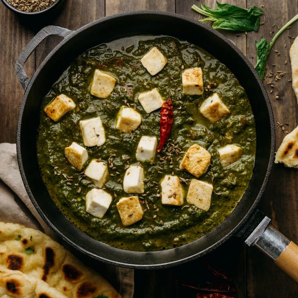 Annapurna Cuisine's Palak Paneer, a vibrant green Indian dish with cheese cubes, spices, and naan.